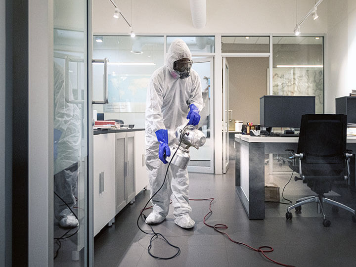 Industrial Hygienists in protective suit, gloves and mask spraying and sanitizing an office space