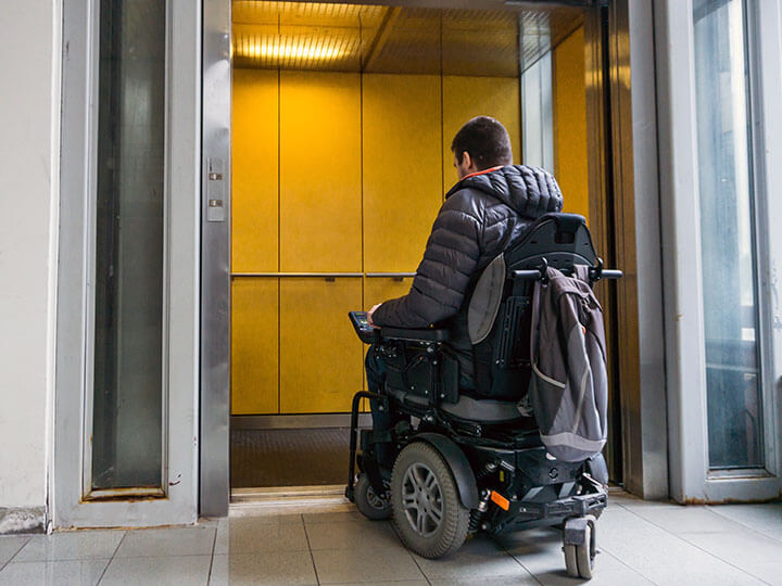 handicapped man in an electric wheelchair waiting to get in an elevator with yellow walls