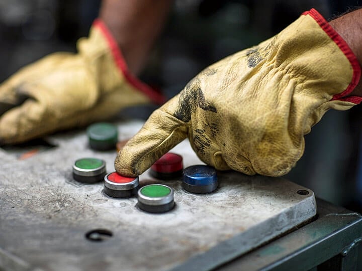 Close up of person wearing cream colored gloves pushing a red button on a control panel with red, blue and green buttons