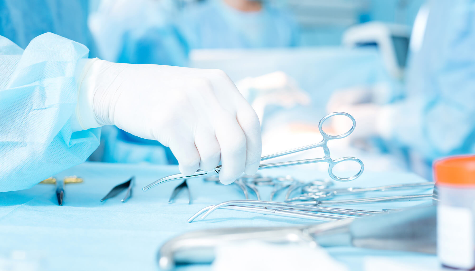 hand wearing white glove picking up a pair of medical scissors