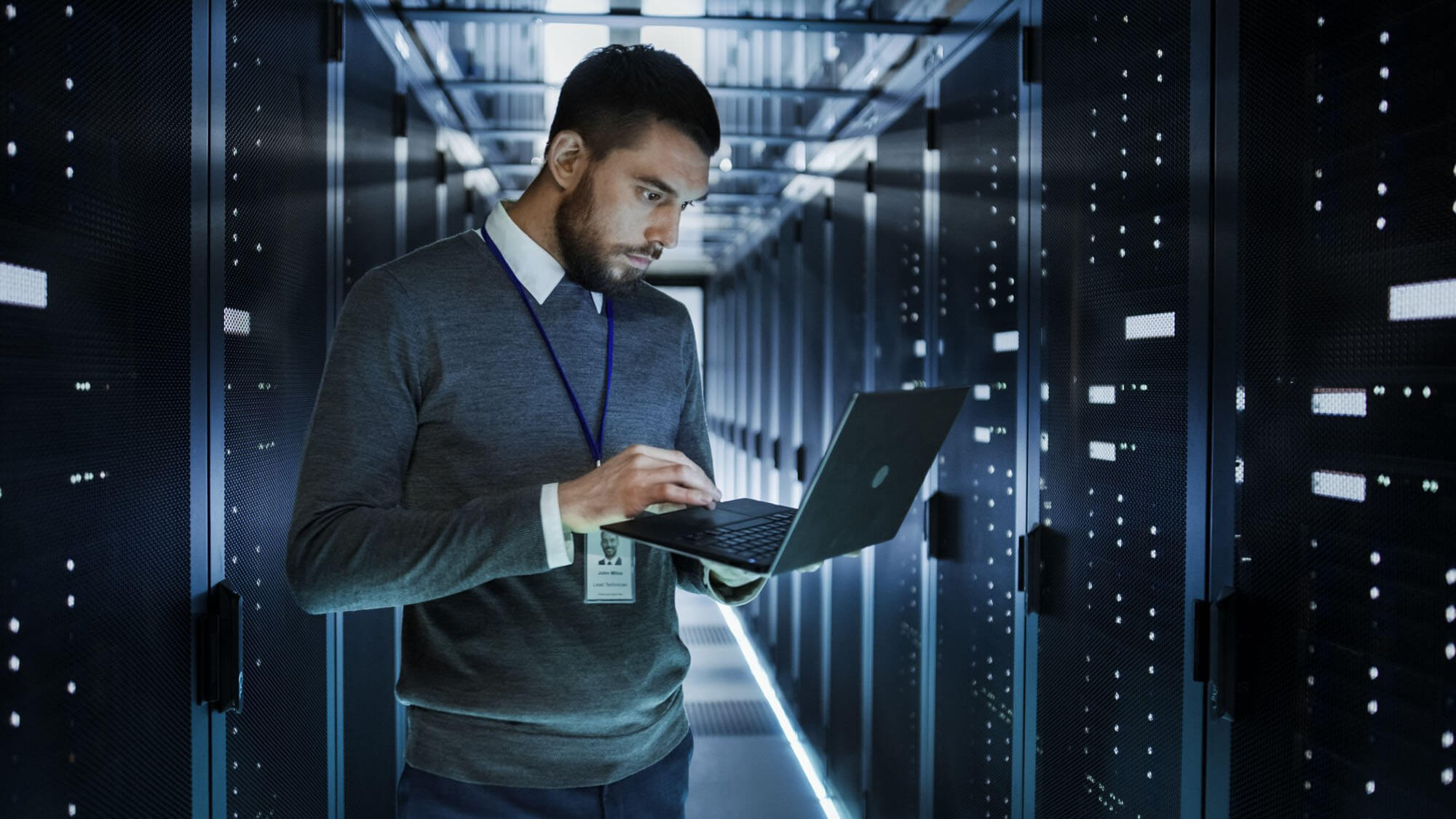 IT technician works on a laptop in big data center full of rack servers